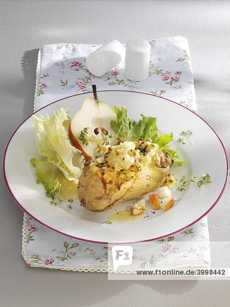 Au gratin potatoes with a pear and salad on a plate with a floral napkin and salt and pepper shakers