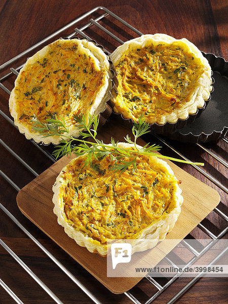 Three carrot tarts in baking trays on a wire cooling rack  decorated with dill