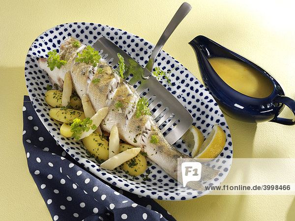 Pike perch with asparagus  potato  lemon  parsley and Riesling sauce in a gravy boat  blue dotted napkin