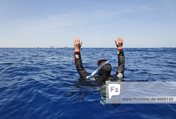 Drifting diver at sea is trying to get the attention of people on dive ships on the horizon by waving Egypt Red Sea Africa