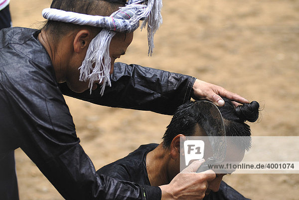 Traditional Basha hair shaving with a sickle on a man with a hair bun of the Basha minority  the smallest minority in China  Basha  Guizhou  China  Asia