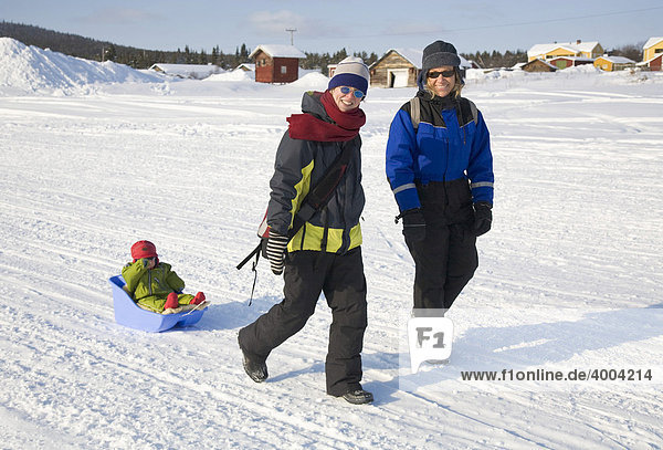 Two women pulling a girl  1  in a sled walking over the frozen river  Torne Aelv  at the edge of the town of Jukkasjaervi  Lappland  North Sweden  Sweden