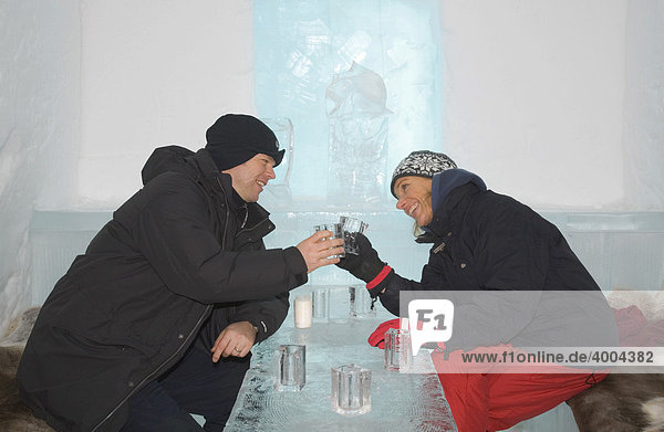 In der Eisbar des Eishotels von Jukkasjärvi stoßen eine Frau und ein Mann mit ihren aus Eis gefertigten Gläsern miteinander an  Jukkasjärvi  Lappland  Nord-Schweden  Schweden