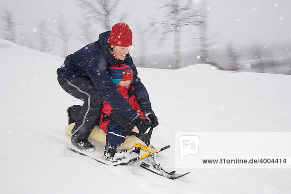 Vierjähriges Mädchen fährt im Schneetreiben mit seiner Mutter auf einem Lenkschlitten einen Abhang hinunter in Kiruna  Lappland  Nord-Schweden  Schweden