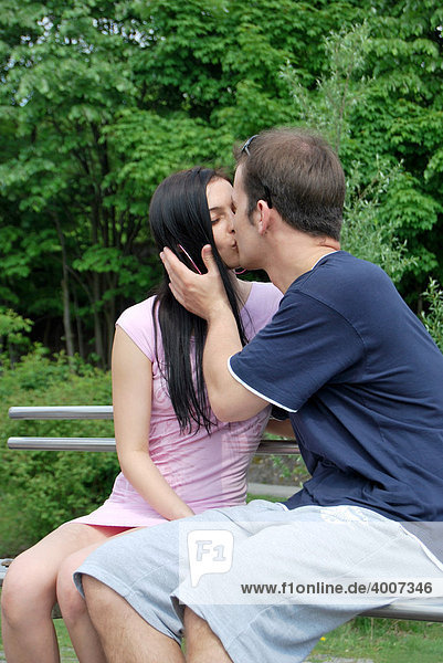 Junges verliebtes Paar  küssend auf einer Parkbank