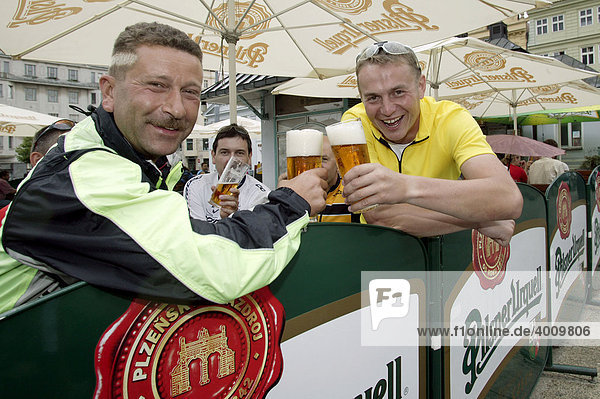 Radfahrer  Männer  stoßen in einem Biergarten auf dem Platz der Republik mit einem Bier an  Pilsner Urquell  an in Pilsen  Plzen  Böhmen  Tschechien  Europa
