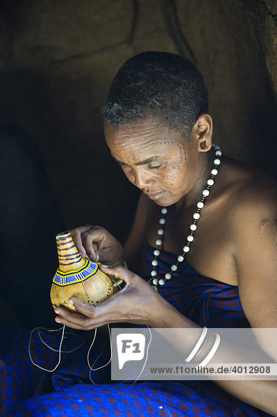 Eine Frau vom Stamm der Datooga dekoriert eine Kalebasse mit Glasperlen Lake Eyassi Tansania Afrika
