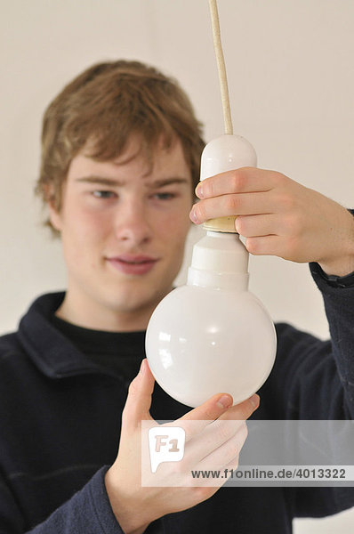 Junger Mann schraubt Energiesparlampe in eine Lampenfasung