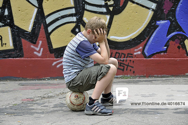 Enttäuschter und einsamer Junge mit seinem Fußball vor einer Graffitiwand  Bolzplatz in Köln  Nordrhein-Westfalen  Deutschland  Europa