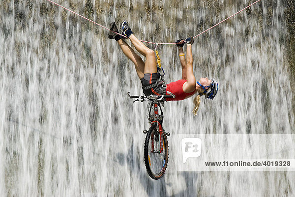 Woman crossing a waterfall on a rope with a bike  Kalkalpen National Park  Upper Austria  Austria  Europe