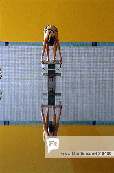 Schwimmerin vor Startsprung von Sockel im Hallenbad mit Spiegelung im Wasser