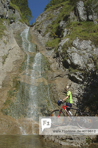 Frau  22 Jahre  mit Mountainbike und Raddress steht an einem Wasserfall  Nationalpark Kalkalpen  Oberösterreich  Österreich  Europa