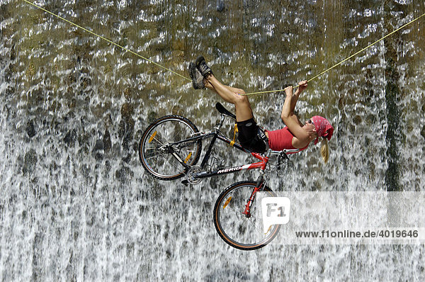 Woman crossing a waterfall on a rope with a bike