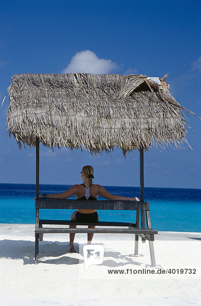 20 year-old woman siting under a thatched roof on a white sand beach looking out over the turquoise sea  Summer Island Village  North Male Atoll  Maldives  Indian Ocean