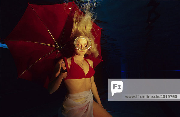 Woman wearing diving goggles and carrying a red umbrella under water in a pool in Losenstein  Upper Austria  Europe