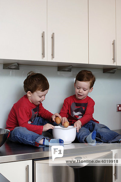 Zwillingsjungen  dreieinhalb Jahre alt  sitzen zum Backen auf der Küchenoberfläche