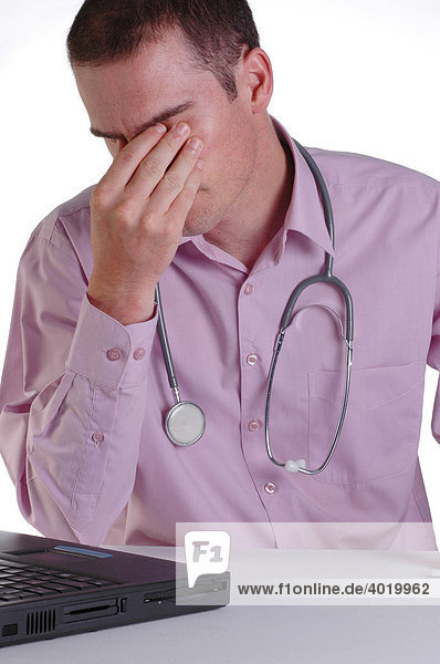 A young male doctor at his desk rubbing his eyes with fatigue from working long hours