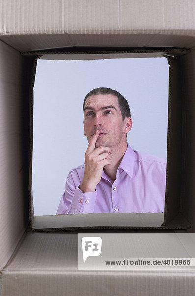 Thoughtful man seen through a box  symbolic for thinking outside the box  creative thought and lateral thinking