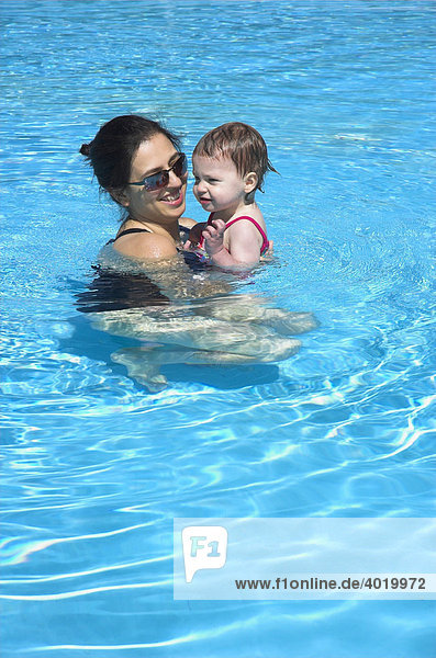 A young mother with her baby daughter playing in a swimming pool