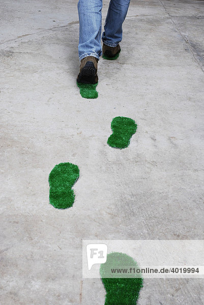 Mann hinterlässt grüne Fußspuren auf einem Betonboden