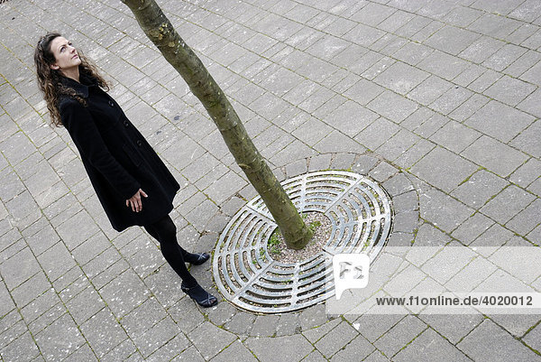 Young woman looking at the trunk of a lone tree in an urban area