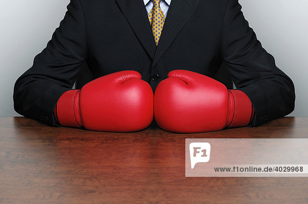 Businessman wearing boxing gloves sat behind a desk