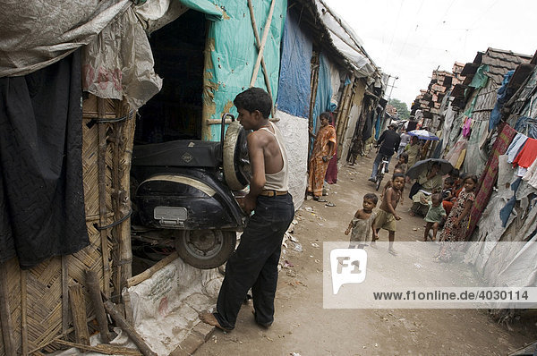 Zwei Jungen tragen in den Slums von Topsia einen Roller in ihre Hütte  solch ein motorisiertes Vehikel zu besitzen  ist hier eigentlich schon ein unerschwinglicher Luxus  Kolkata  Westbengalen  Indien