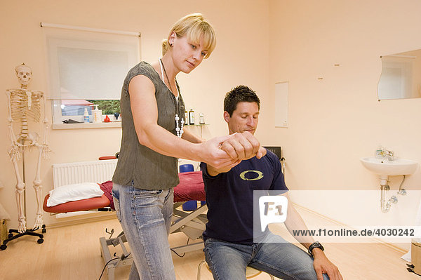 Physiotherapeutin  Lehrerin für Alexandertechnik führt mit einem Patienten eine Entspannungsübung zur Steigerung der Greiffähigkeit im Praxisraum durch