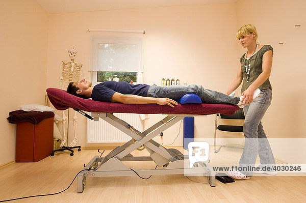 Physiotherapeutin  Lehrerin für Alexandertechnik führt mit einem Patienten eine Entspannungsübung der Füße im Praxisraum durch