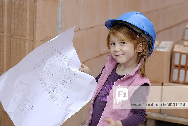 Mädchen mit Bauhelm studiert Bauplan in einem Rohbau auf einer Baustelle