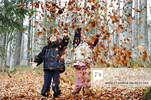 Kinder spielen im Herbst mit Laub