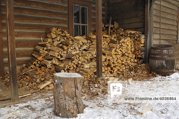 Wood pile and chopping block outside a cabin in the winter  Fort Edmonton Park  historical recreation tourist attraction  Edmonton  Alberta  Canada