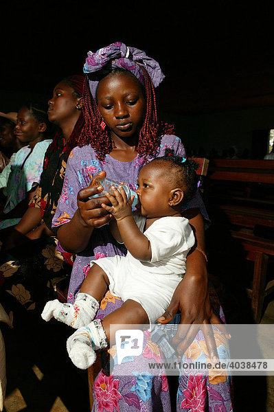 Woman feeding an infant with a bottle  during church service  Manyemen  Cameroon  Africa
