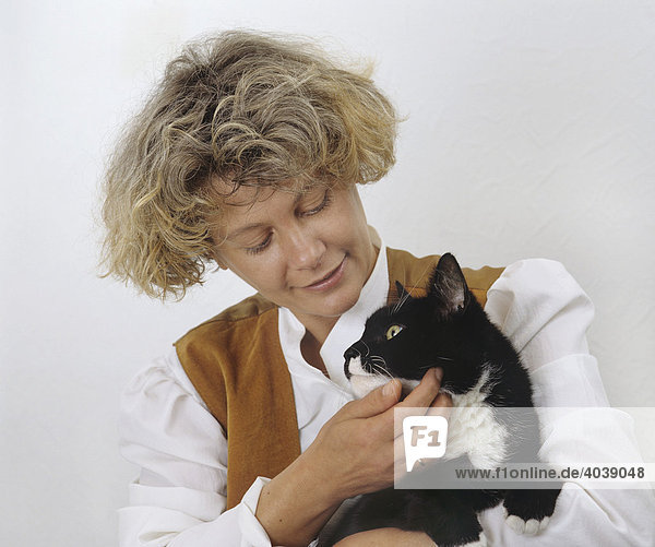 Frau hält schwarz-weiße Katze auf dem Arm und krault diese liebevoll unterm Kinn