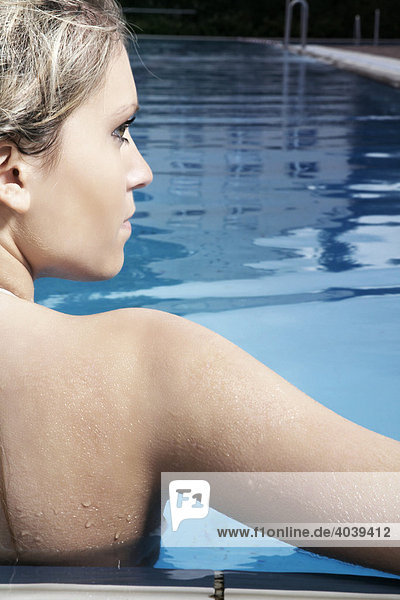 Junge dunkelblonde Frau lehnt am Beckenrand im Schwimmbad