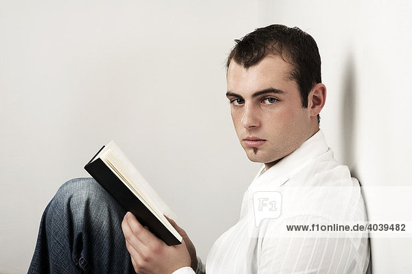 Junger Mann hält ein Buch in der Hand und blickt dabei in die Kamera