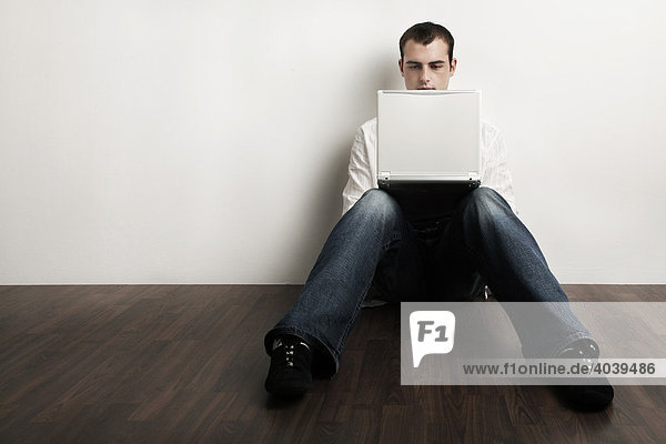 Young man sitting on the floor working on his laptop