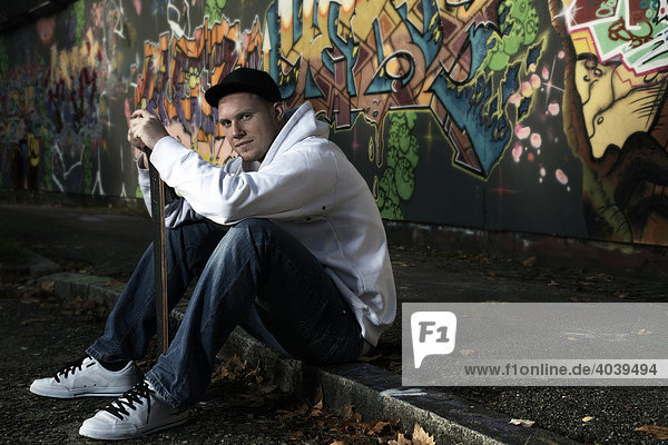 Junger Mann mit Skateboard vor einer Graffitiwand