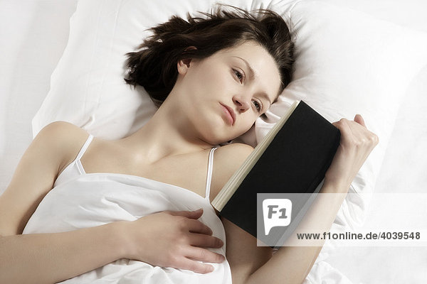 Junge brünette Frau liest ein Buch im Bett