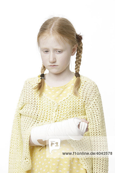 8-jähriges Mädchen mit Haarzöpfen und gebrochenem Arm in Gips  traurig  sieht auf Boden