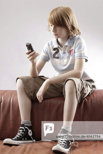 12-jähriger Junge sitzt auf Sofa  mit Handy