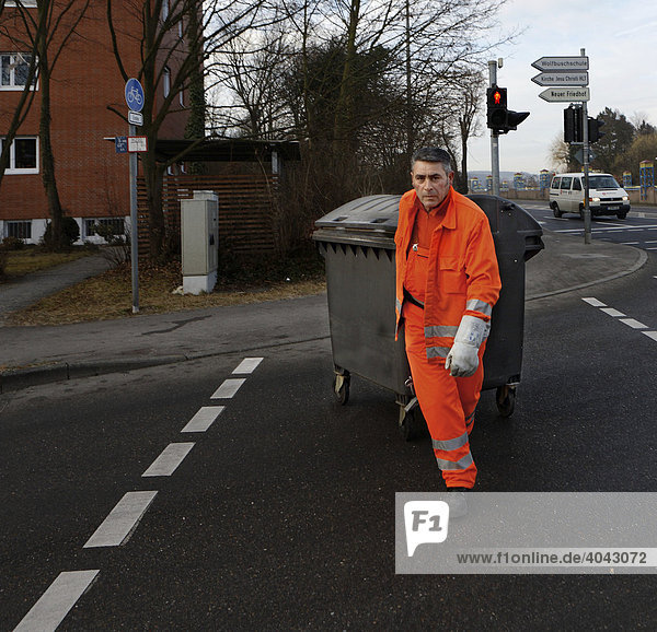 Garbage collector for the Stuttgart garbage company  called AWS or Abfallwirtschaft Stuttgart  pulling a garbage container across a pedestrian crossing through a red traffic light  Stuttgart  Baden-Wuerttemberg  Germany  Europe