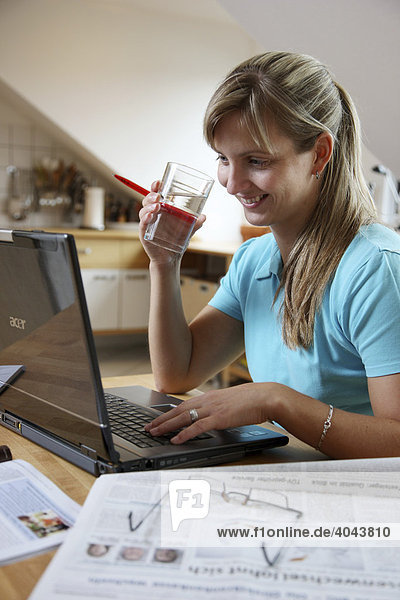 Junge Frau  25-30 Jahre  surft mit Laptop Computer im Internet am Küchentisch