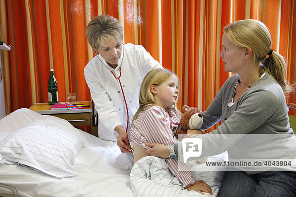 Ärztin untersucht eine junge Patientin  7 Jahre  gestützt von der Mutter  im Krankenbett in einem Krankenhaus