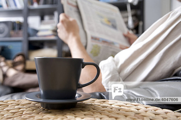Kaffeetasse  dahinter liest ein Mann Zeitung