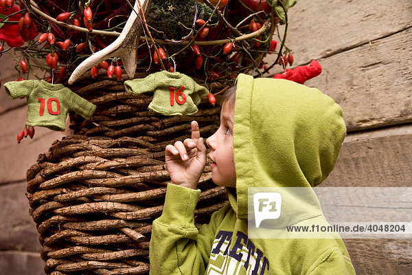 Kleiner Junge steht an der Holzwand einer Wanderhütte mit Weihnachtsdekoration