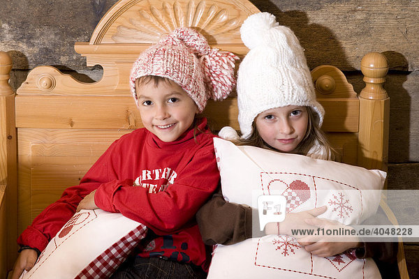 Zwei Geschwister-Kinder sitzen auf alter Bank in einer Wanderhütte