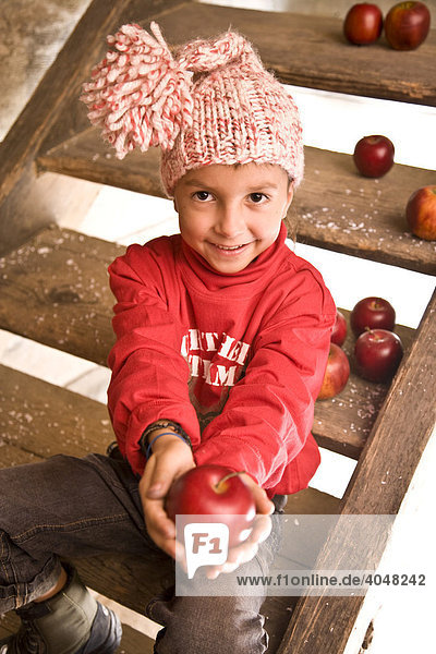 Ein Junge sitzt auf der Treppe einer Wanderhütte und hält einen Apfel in der Hand
