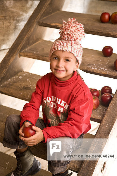 Ein Junge sitzt auf der Treppe einer Wanderhütte und hält einen Apfel in der Hand