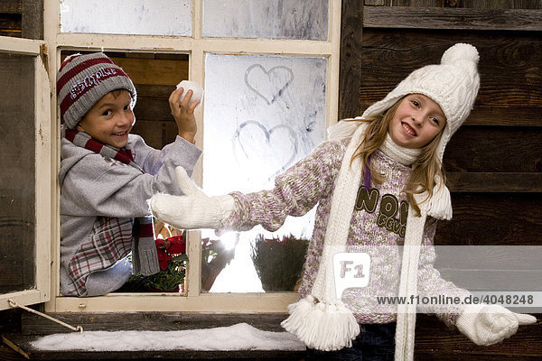 Zwei Geschwister-Kinder spielen am Fenster einer Wanderhütte